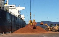 Ships cranes and clamshell grabs at work whilst front end loaders heap up the bauxite for faster loading